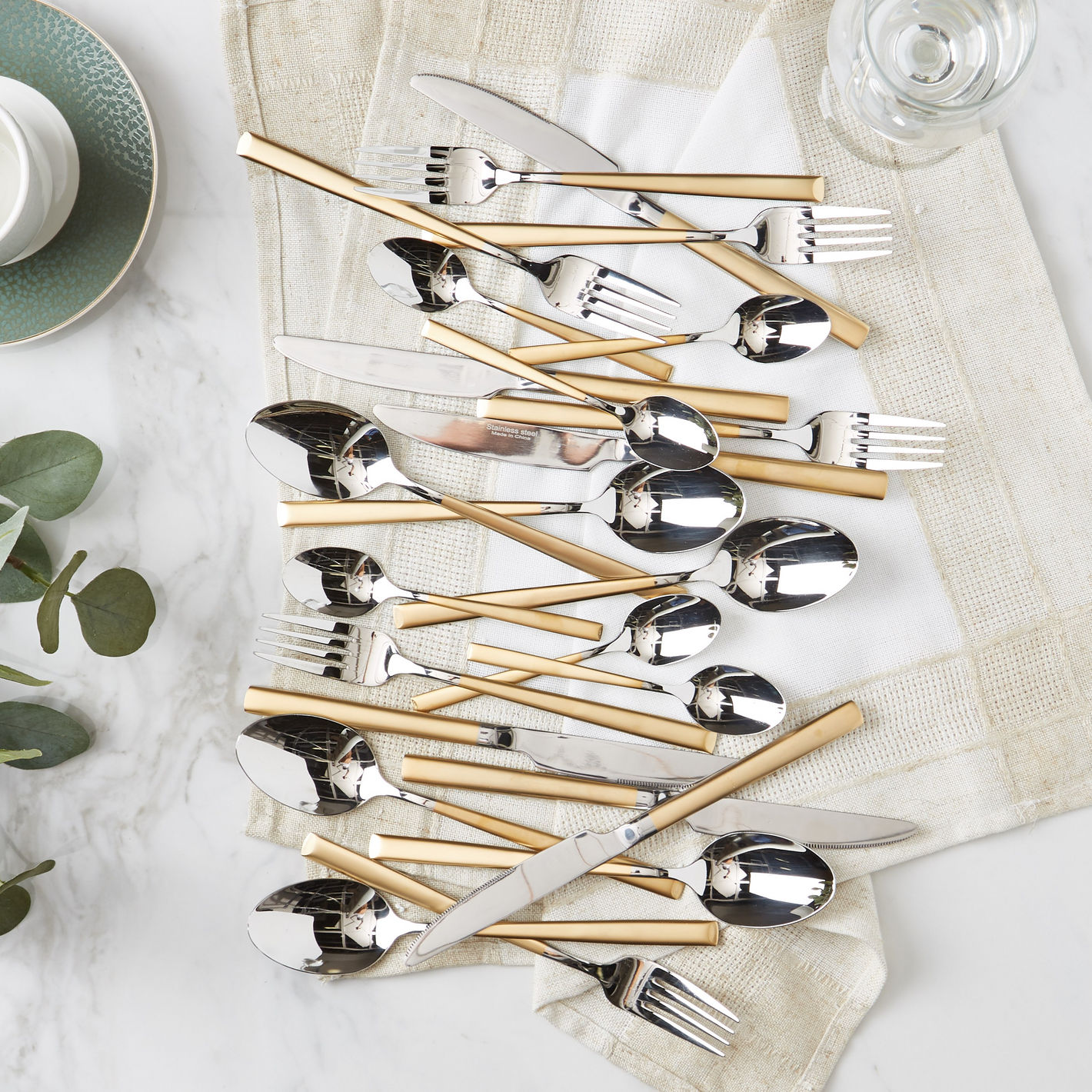 Set of silver cutlery with gold handles on a white surface with a beige napkin.