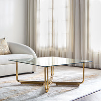 Modern glass coffee table with gold legs in a living room setting