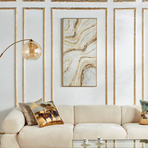 Beige sofa with decorative pillows in a living room setting with wall art and lamp.