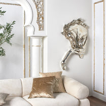 Decorative wall sculpture above a white sofa with gold cushions in a stylish room.