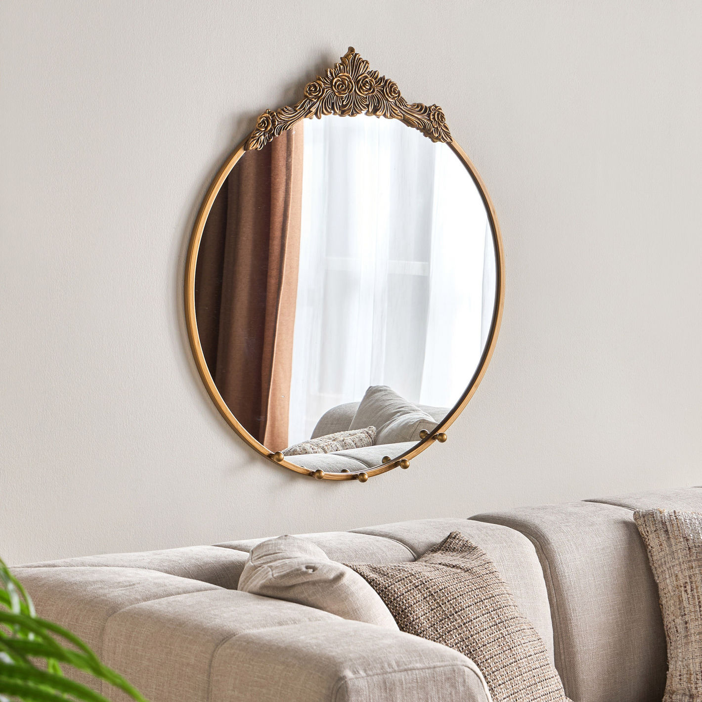 Decorative round mirror with gold frame on a wall above a sofa.