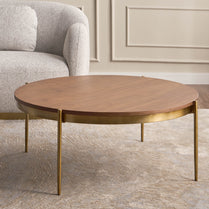 Round wooden coffee table with gold legs in a living room setting
