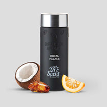 Black diffuser aroma bottle with silver cap, surrounded by a coconut, amber stone, and orange slice on a light gray background.