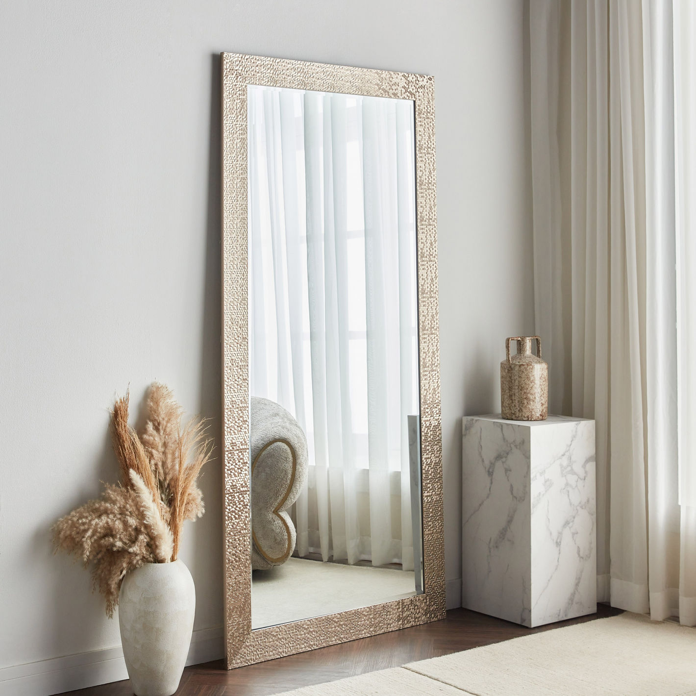 Decorative full-length mirror with a textured frame in a room setting.