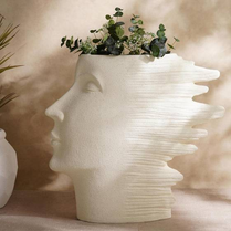 White face-shaped vase with greenery on a neutral background