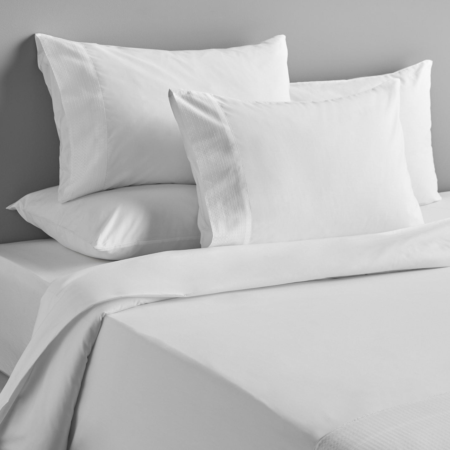 Gray bedding set with pillows on a bed against a gray wall.
