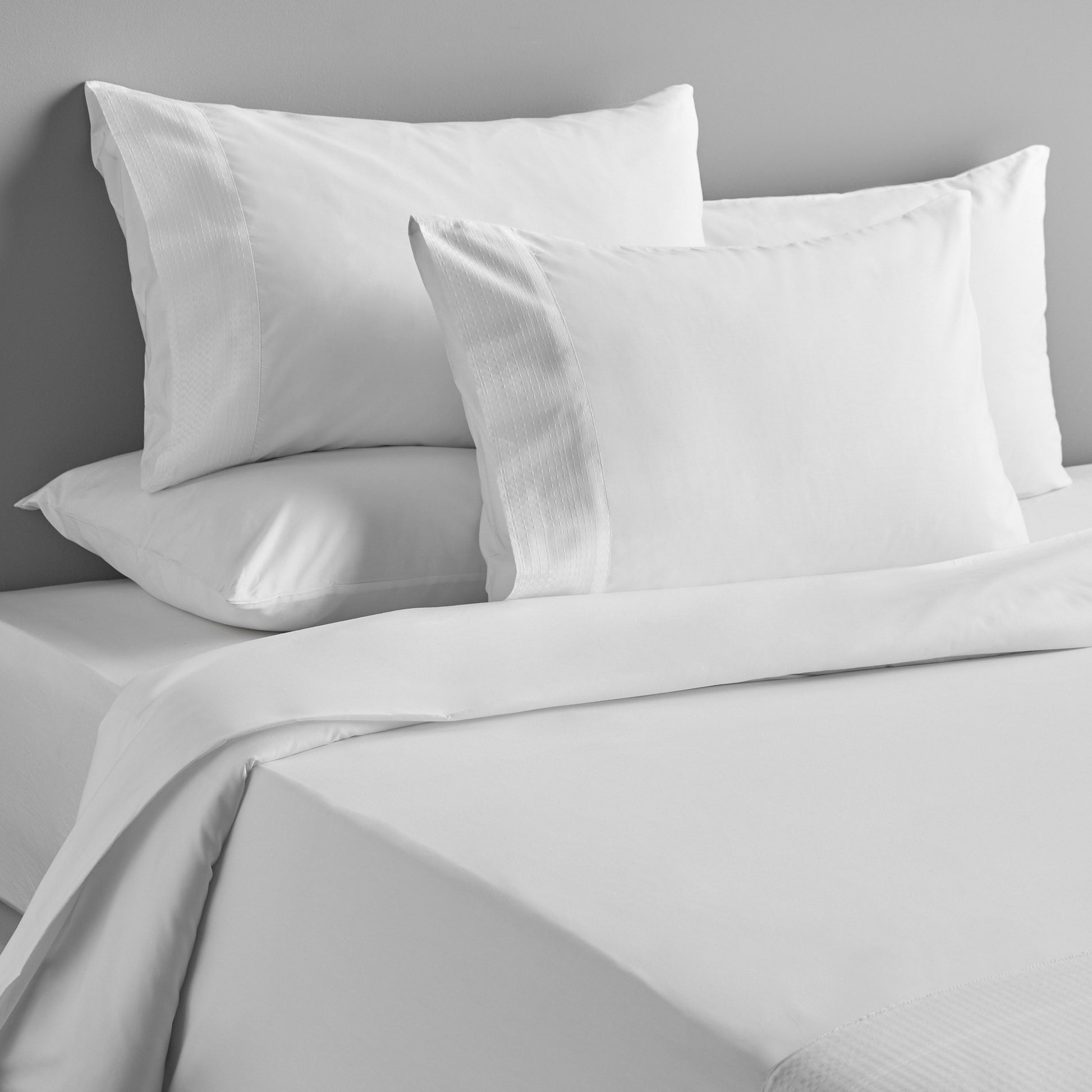 Gray bedding set with pillows on a bed against a gray wall.