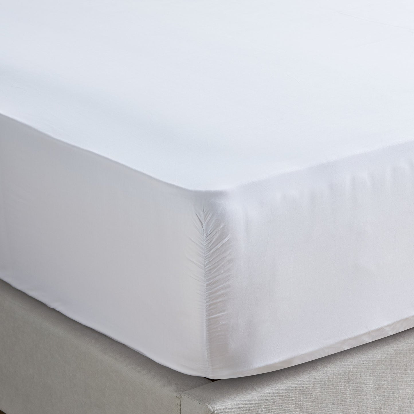 White fitted sheet on a bed with a light gray headboard.