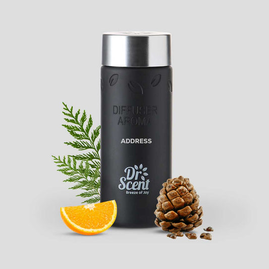 Black diffuser aroma bottle with silver cap, surrounded by green leaves and an orange slice on a light gray background.