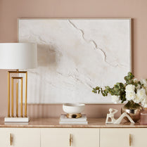 Decorative setup with a marble-patterned painting, lamp, and sculptures on a beige surface.