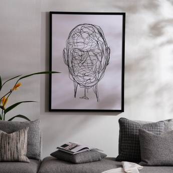 Framed abstract art of a face on a wall above a sofa with decorative pillows.