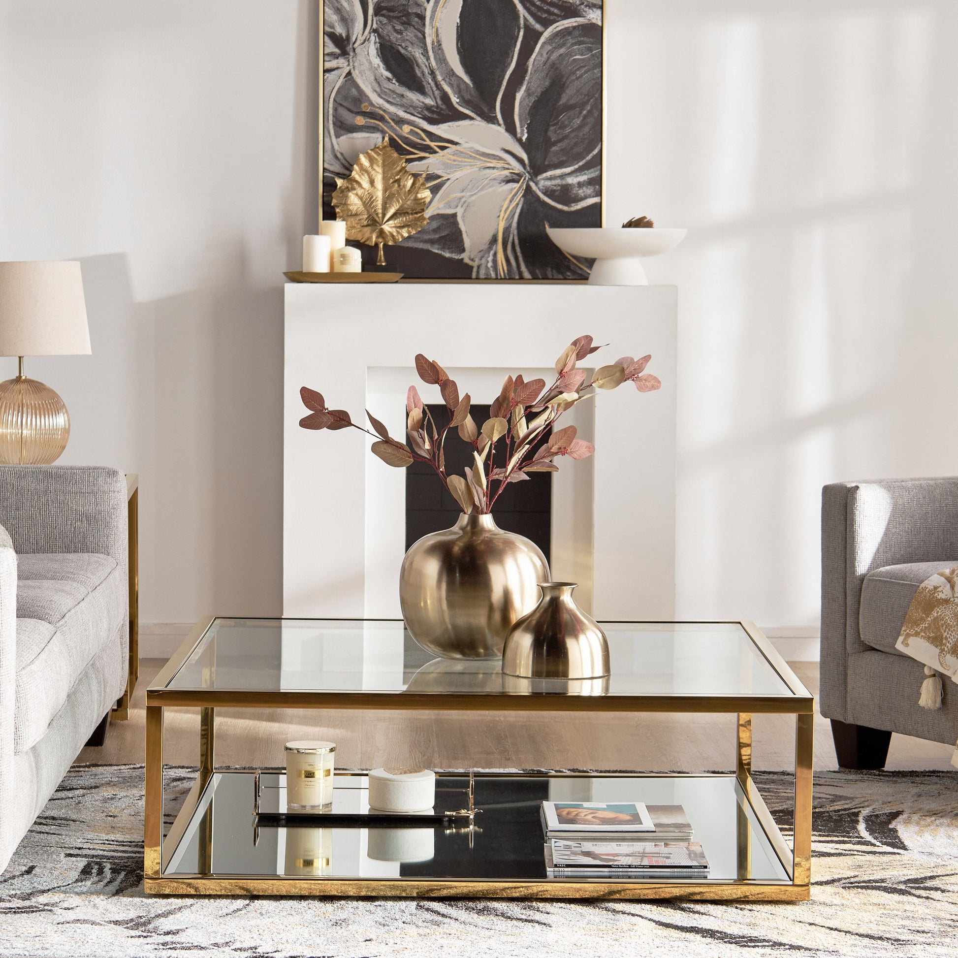 Modern living room with a glass coffee table, gold vase, and decorative elements.