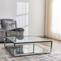 Glass coffee table in a living room with a gray armchair and white walls.