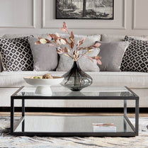 Living room with a glass coffee table, vase with flowers, and decorative items.