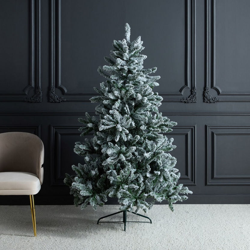 Frosted artificial Christmas tree in a room with dark paneled walls and a beige chair.
