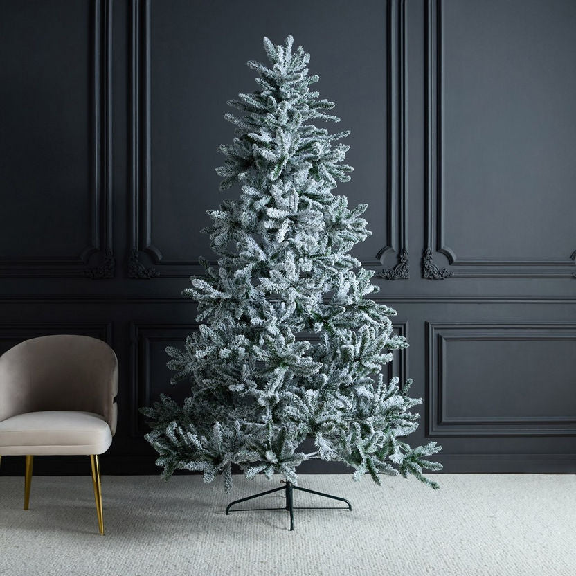 Frosted artificial Christmas tree in a room with dark paneled walls and a beige chair.