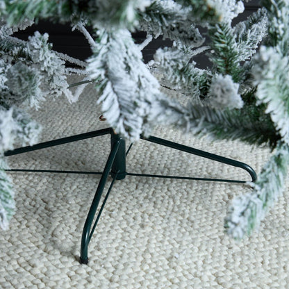 Frosty artificial Christmas tree on a stand with a textured beige surface background