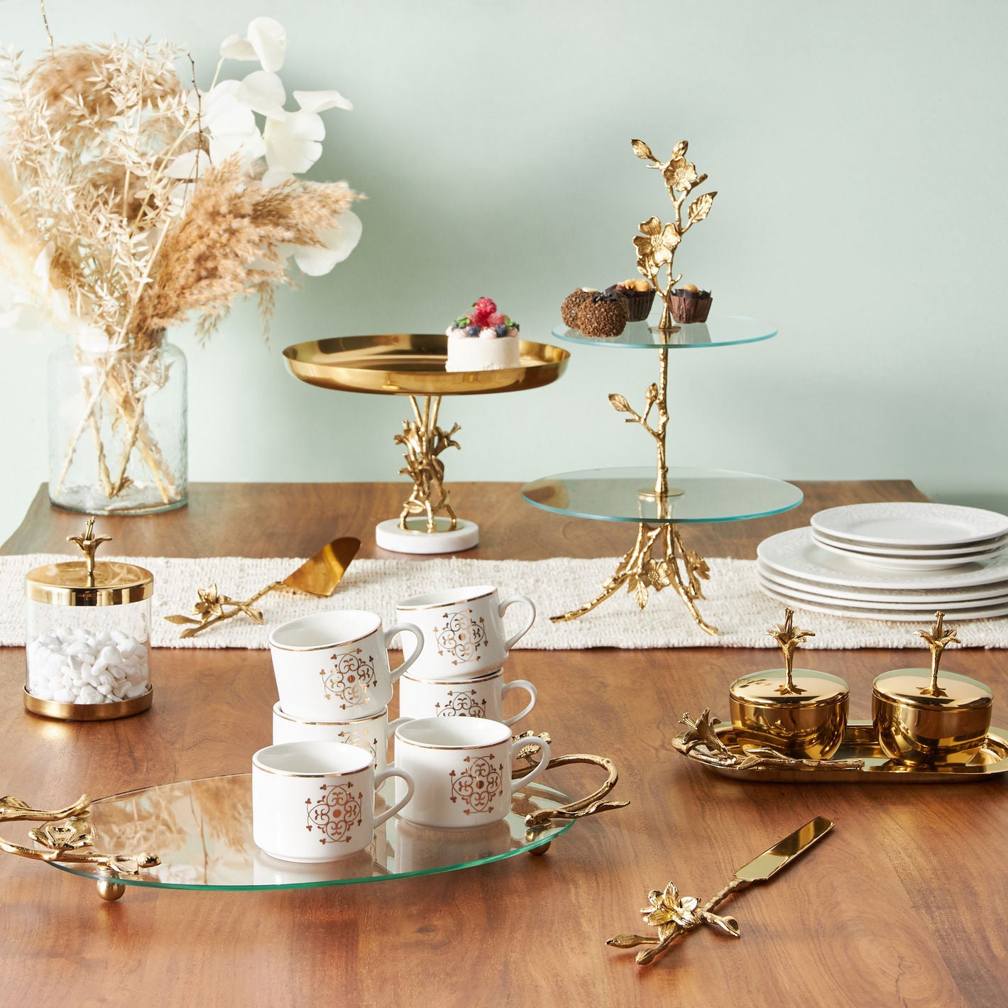 Decorative table setting with gold and white tea cups, plates, and serving trays on a wooden table.