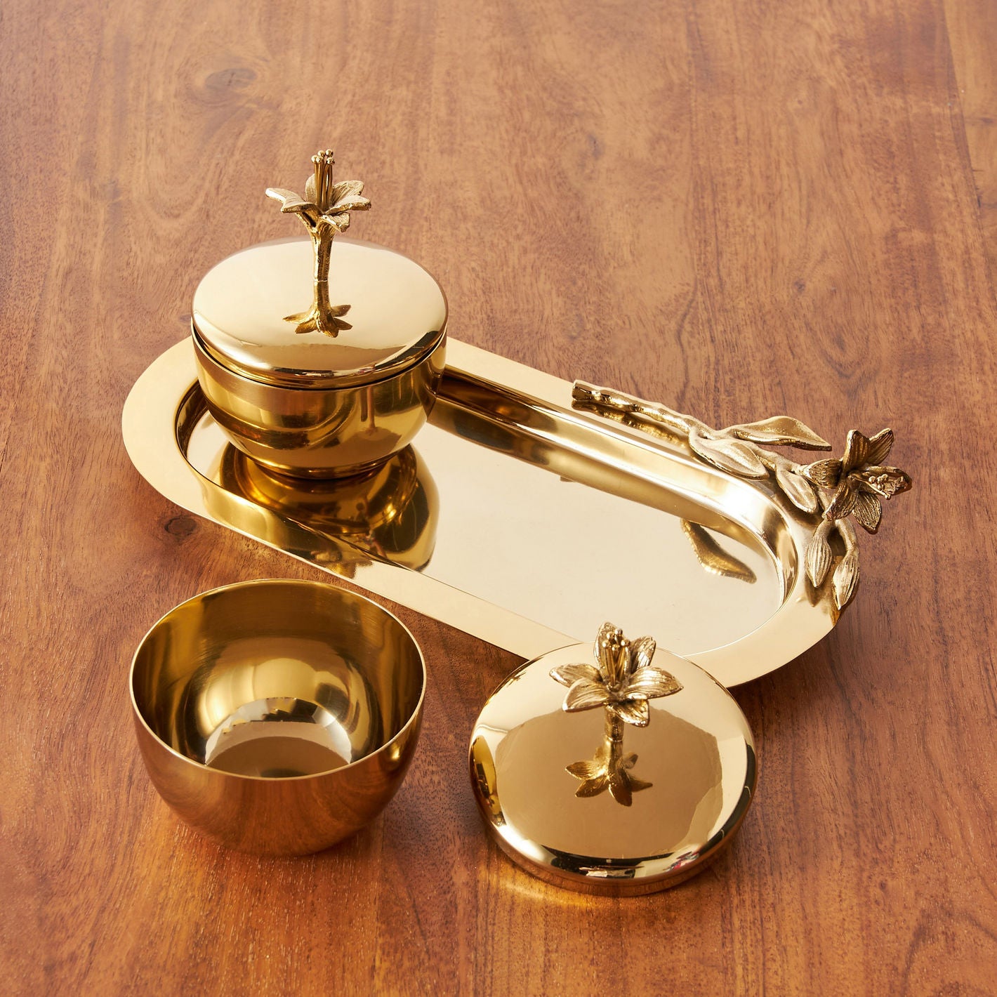 Set of gold decorative items including a tray, bowls, and lids on a wooden surface
