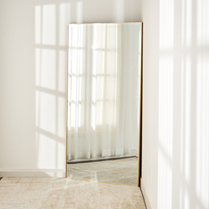 Full-length mirror with gold frame in a minimalistic room.