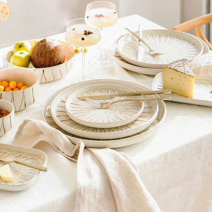 White ceramic plates and bowls on a table with fruits and cheese