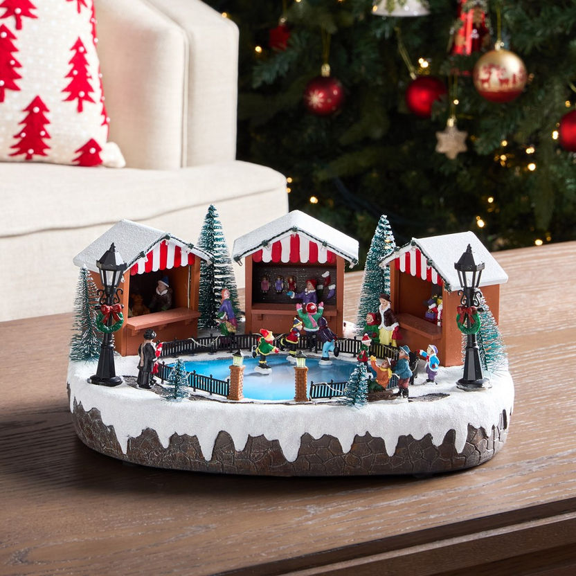 Christmas-themed ice skating rink ornament with people and trees on a wooden surface.