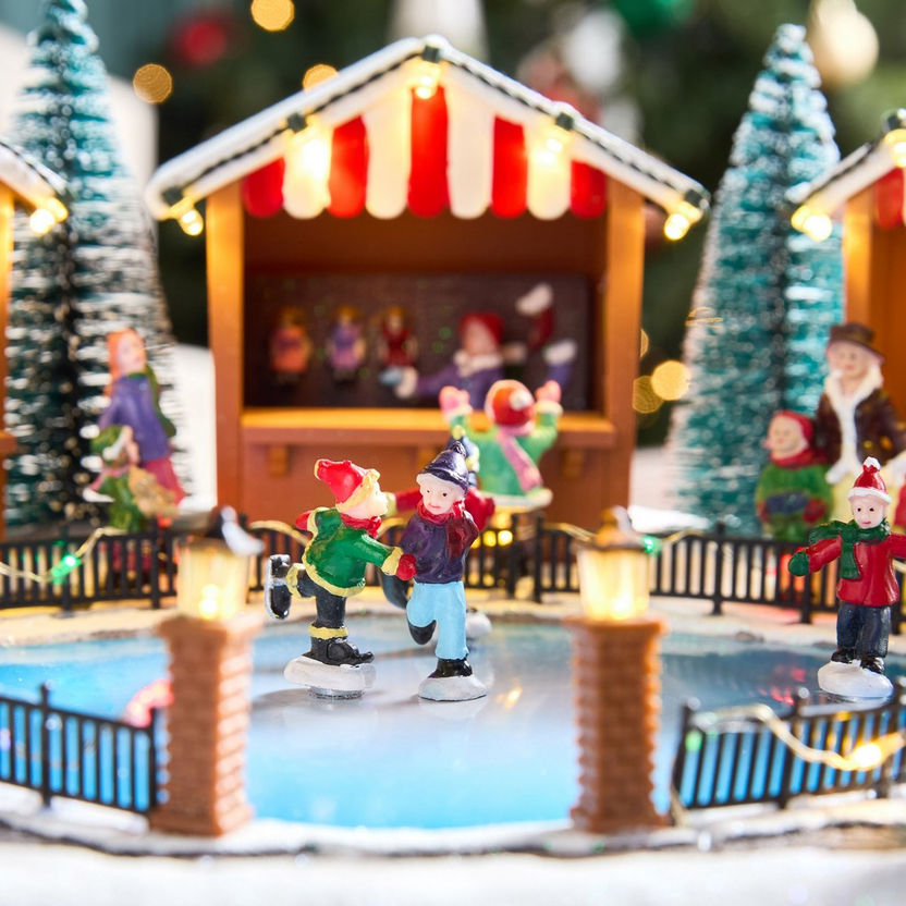 Miniature ice skating rink scene with figures and a carousel in a festive setting.