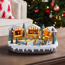 Decorative ice skating rink scene with small buildings and people on a wooden surface.