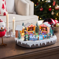 Gingerbread house scene with ice skating rink and Christmas decorations on a table.
