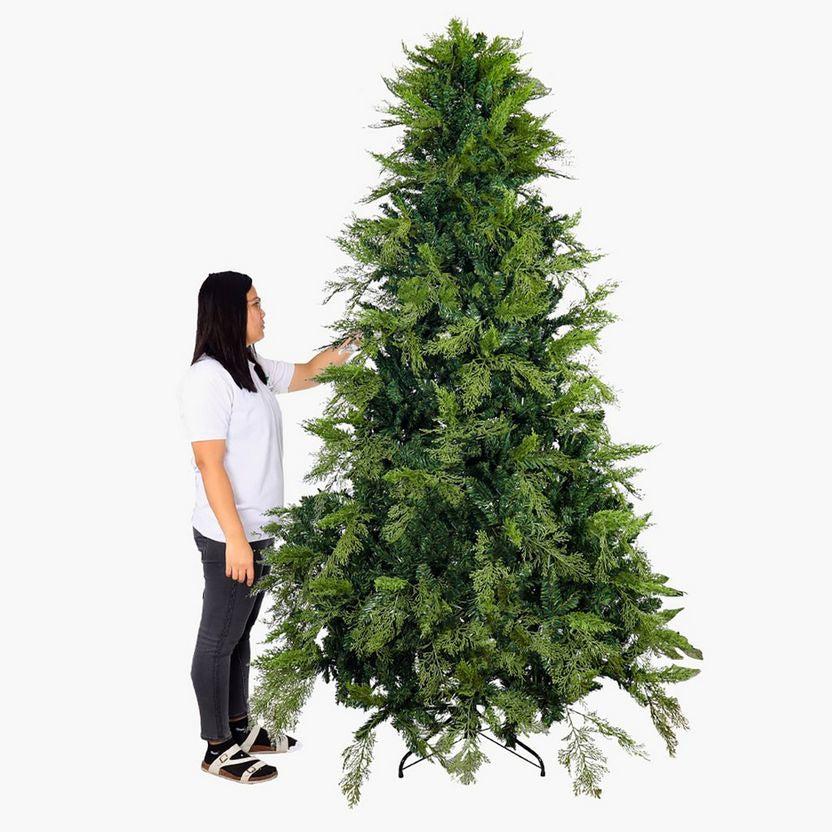 Woman standing next to a tall artificial Christmas tree on a white background