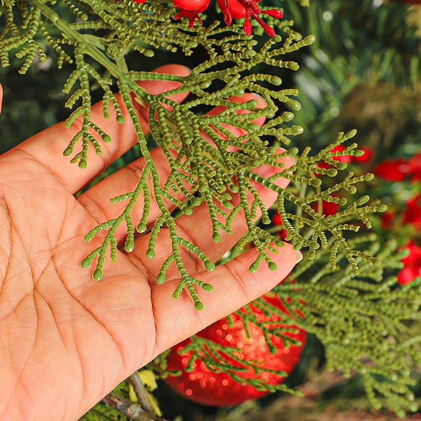 Hand holding a branch of greenery with red berries against a blurred natural background