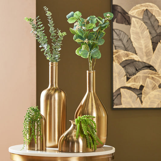 Gold vases with green plants on a marble surface against a brown wall with abstract art.