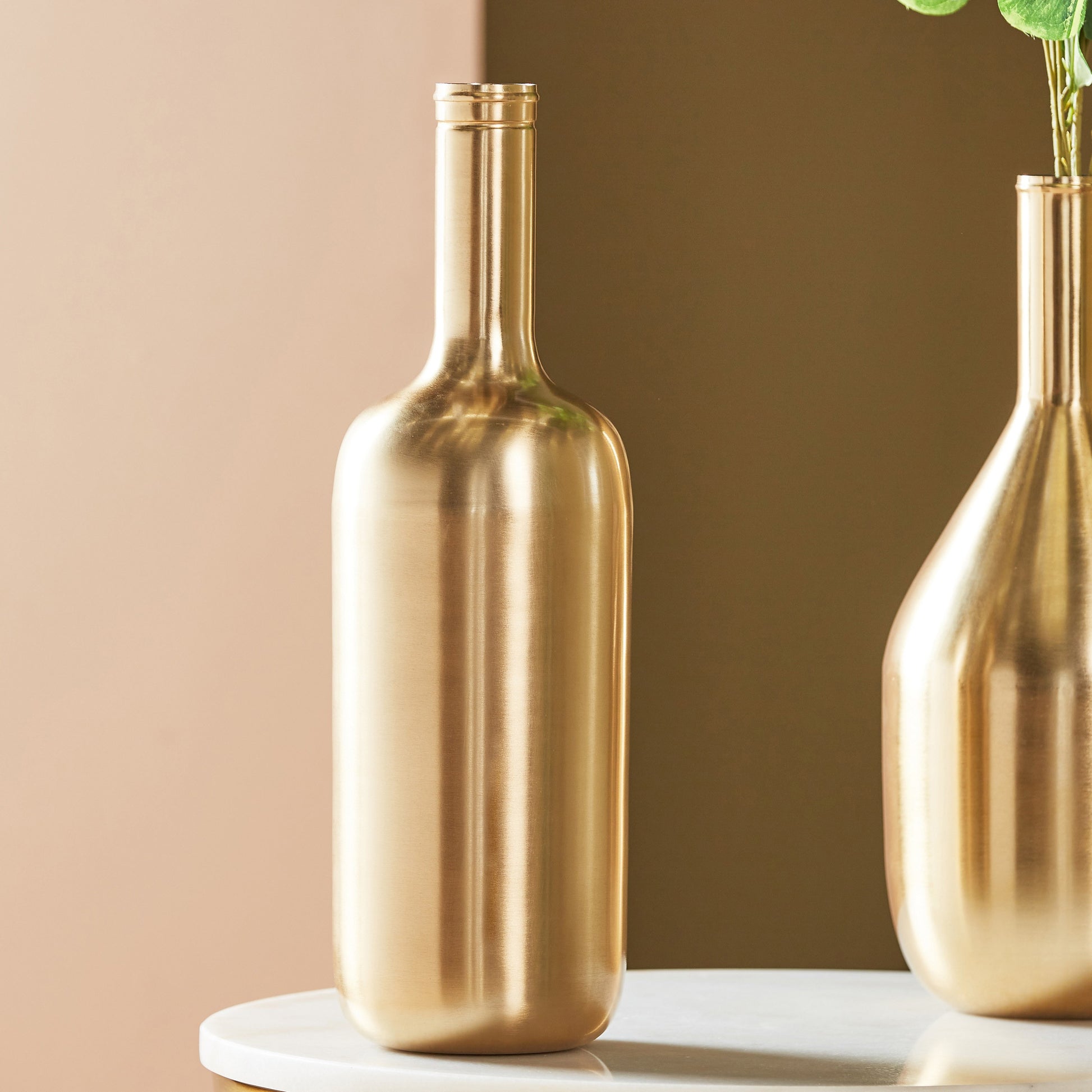 Two gold bottle-shaped vases on a white surface with a beige background