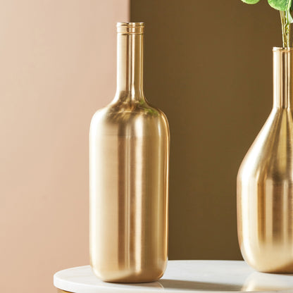 Two gold bottle-shaped vases on a white surface with a beige background