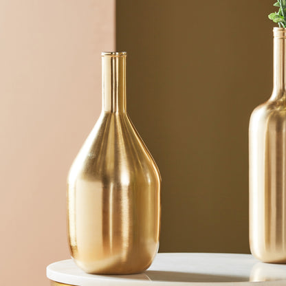 Two gold vases on a white surface with a beige background