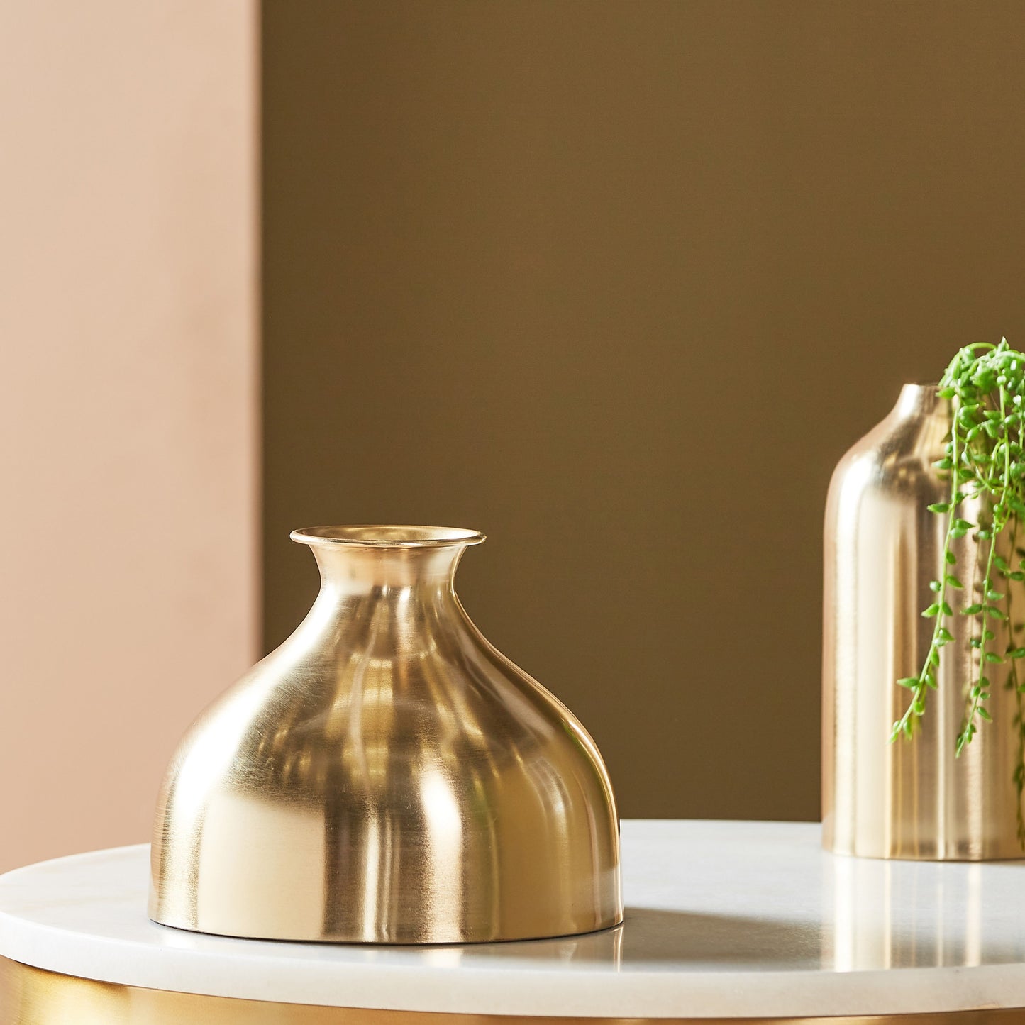 Two gold vases on a white surface with a brown wall background