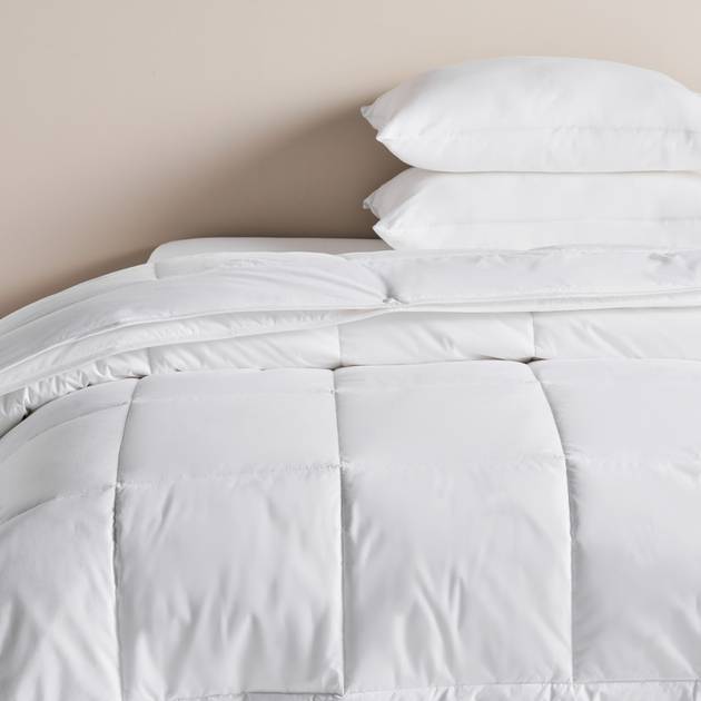 White comforter and pillows on a bed against a beige wall
