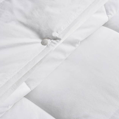 Close-up of a white quilt with a button detail on a light gray background