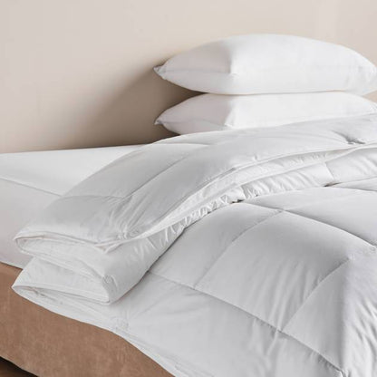 White comforter and pillows on a bed with a beige wall background
