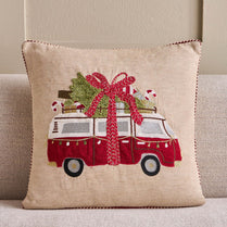 Decorative pillow with a red van carrying a Christmas tree on a beige background