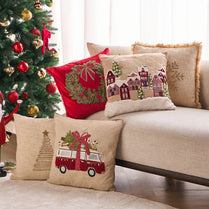 Decorative pillows with Christmas-themed designs on a couch next to a decorated tree.