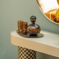 Decorative glass decanter and tumblers on a table with a mirror reflecting the scene.