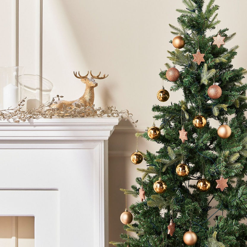 Decorated Christmas tree with gold and bronze ornaments next to a fireplace with a gold deer ornament.