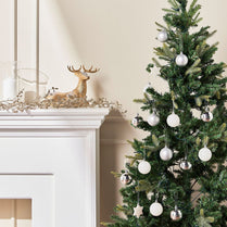 Decorated Christmas tree with ornaments next to a fireplace with a gold deer decoration.