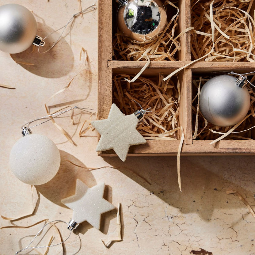 Decorative Christmas ornaments including silver balls and beige stars on a textured surface with straw.
