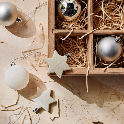 Decorative Christmas ornaments including silver balls and beige stars on a textured surface with straw.