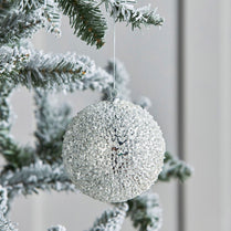 Silver glittery Christmas ball ornament hanging on a tree branch with snow.