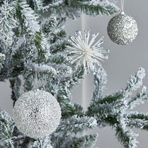 Decorative Christmas tree with silver glittery ornaments against a neutral background