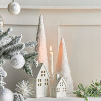 Christmas decor with white houses, trees, and candle on a neutral background