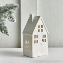White ceramic house-shaped lantern on a white surface with a light interior